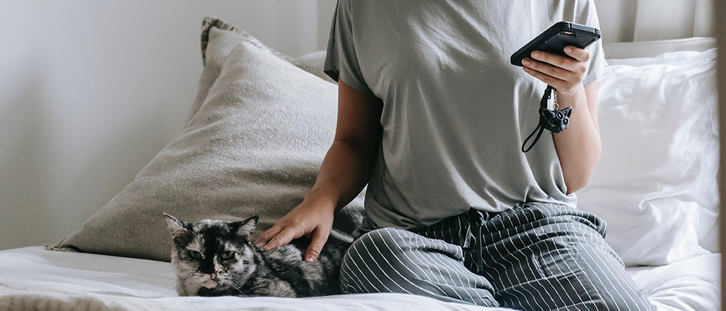 Femme assise caressant un chat et utilisant son smartphone sur un matelas en latex naturel