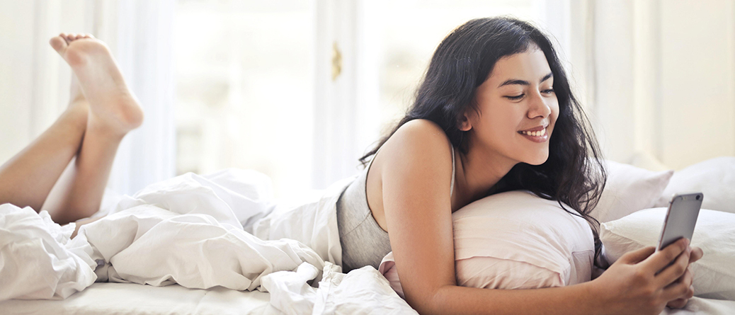 Femme allongée sur son matelas latex naturel avec son téléphone à la main