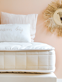 Matelas Le Petit Cosme enfant, posé sur un sommier, avec deux oreillers de décoration sur le dessus