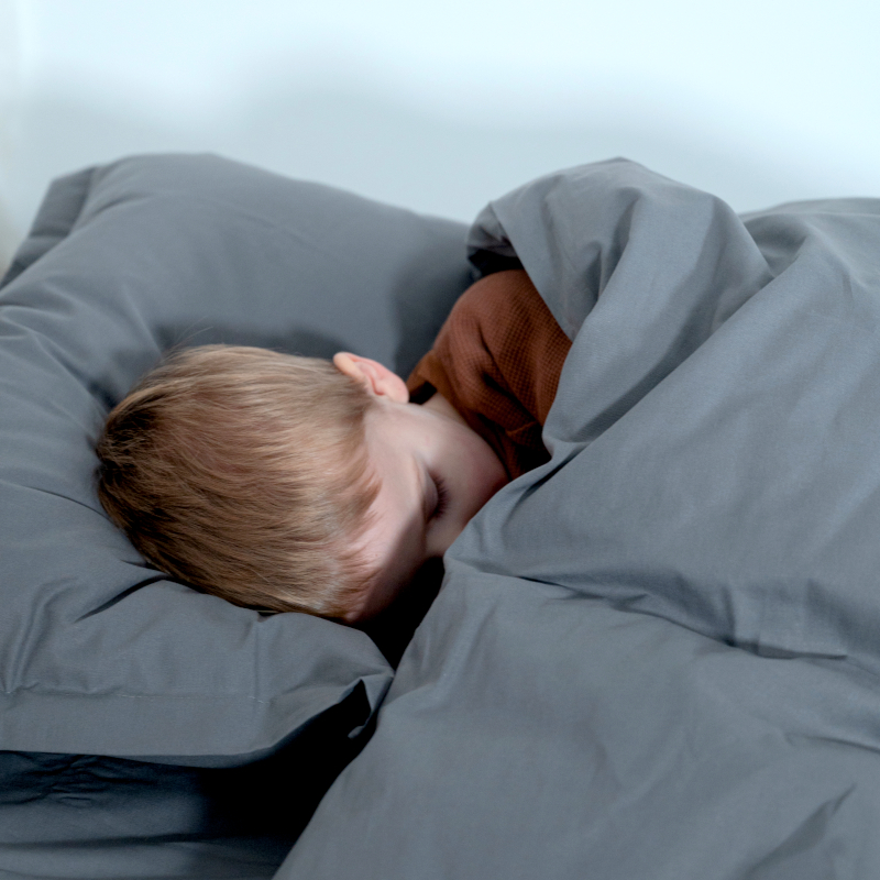 image représentant un enfant dormant dans un lit composé d'une parure de lit en coton bio gris