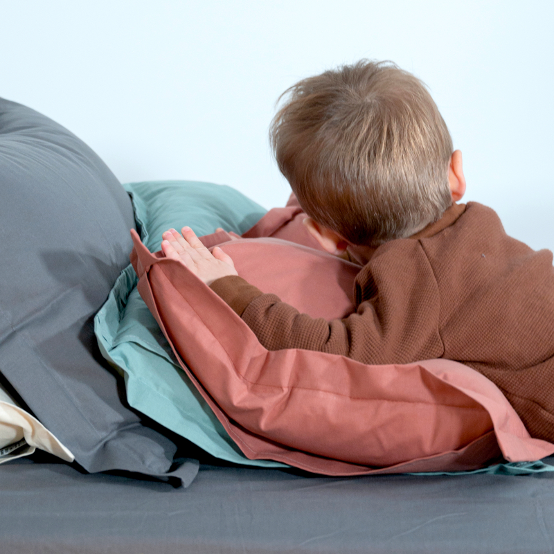 image représentant un enfant allongé sur des oreillés avec des taies d'oreillé en coton bio terracota, vert d'eau, gris