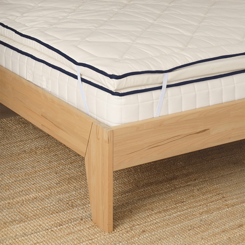 Surmatelas Cosme roulé et rangé facilement à côté d'un canapé.